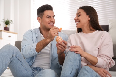 Photo of Happy man feeding girlfriend with tangerine at home