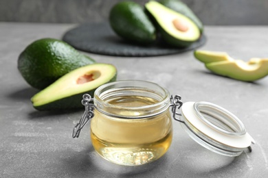 Photo of Jar of natural oil and avocados on grey stone table