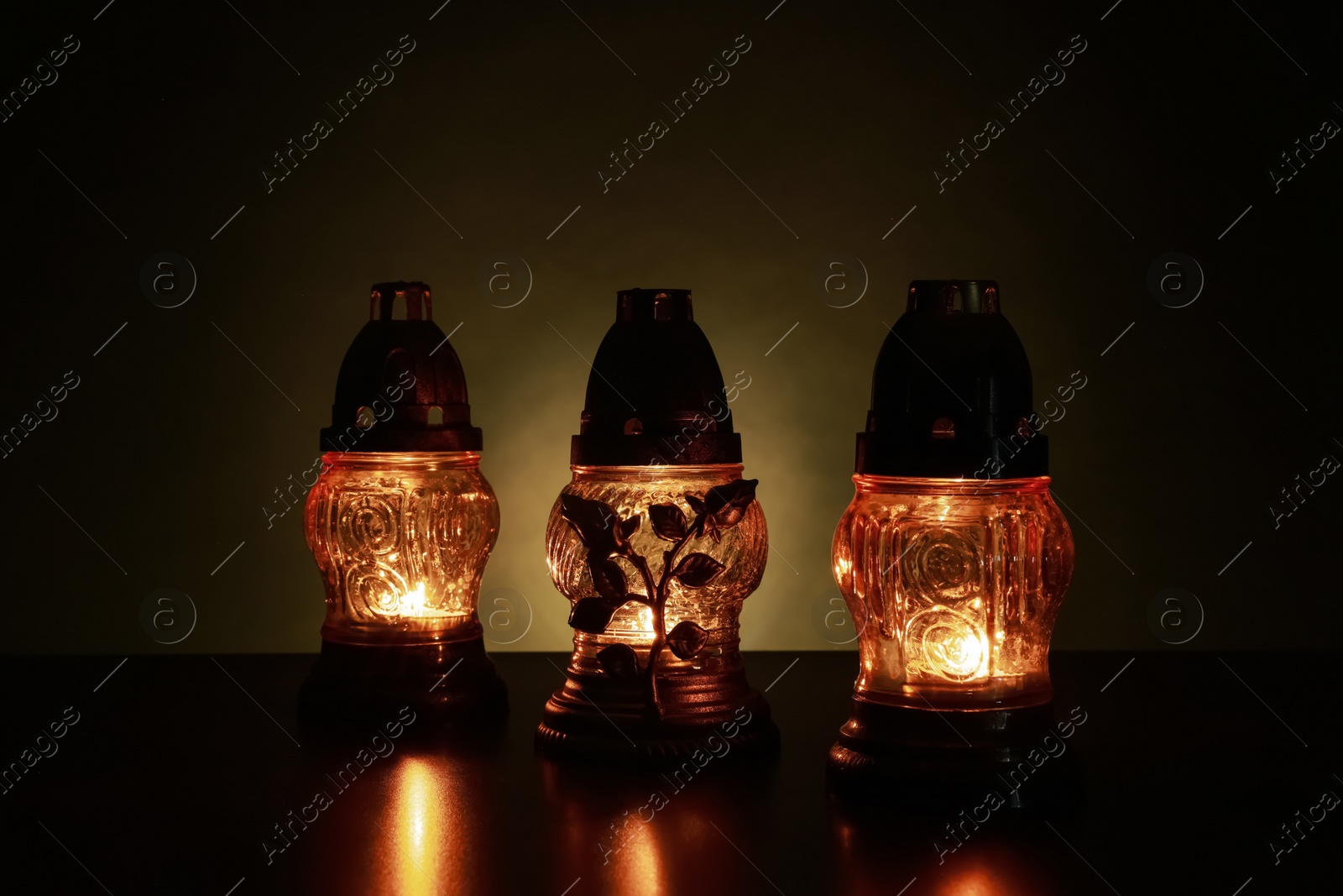 Photo of Beautiful glowing grave lights on table in darkness. Symbol of remembrance