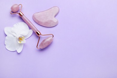 Photo of Gua sha stone, face roller and orchid flower on violet background, flat lay. Space for text