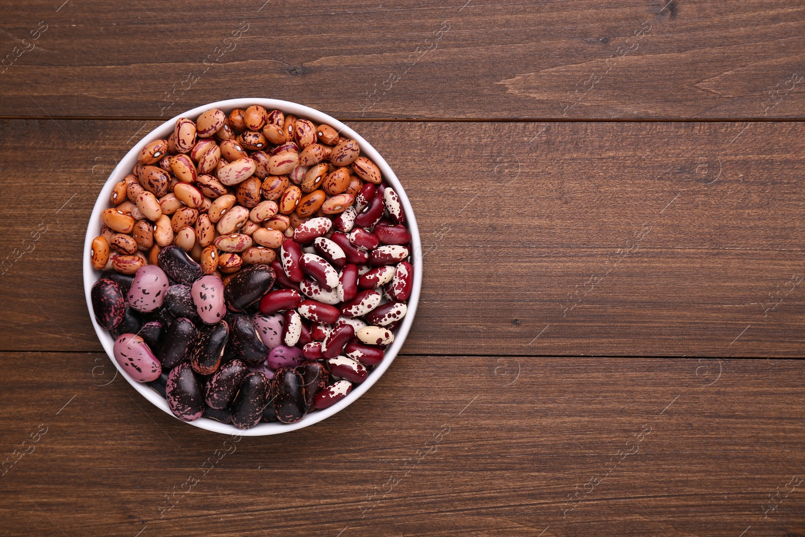 Photo of Different kinds of dry kidney beans in bowl on wooden table, top view. Space for text