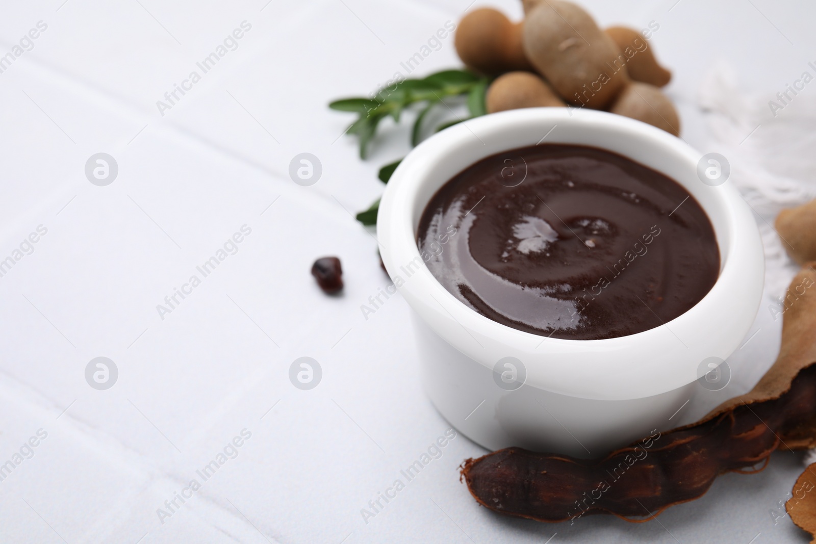 Bowl of tasty tamarind sauce and fresh pods on white table. Space for text Photo of Bowl of tasty tamarind sauce and fresh pods on white table. Space for text