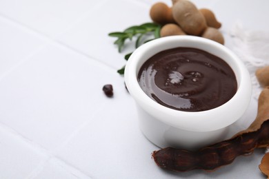 Photo of Bowl of tasty tamarind sauce and fresh pods on white table. Space for text