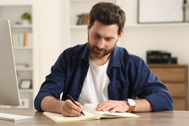 Photo of Home workplace. Happy man taking notes at wooden desk in room