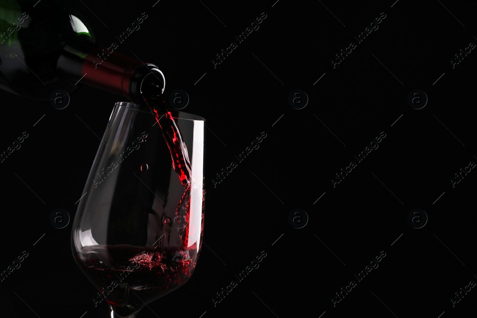 Photo of Pouring tasty red wine from bottle into glass on black background, closeup. Space for text