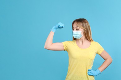 Woman with protective mask and gloves showing muscles on light blue background, space for text. Strong immunity concept