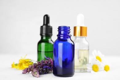 Photo of Bottles of different essential oils and wildflowers on light table