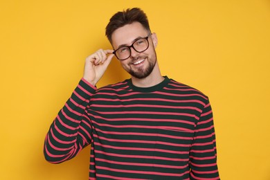 Handsome man in striped sweatshirt and eyeglasses on yellow background