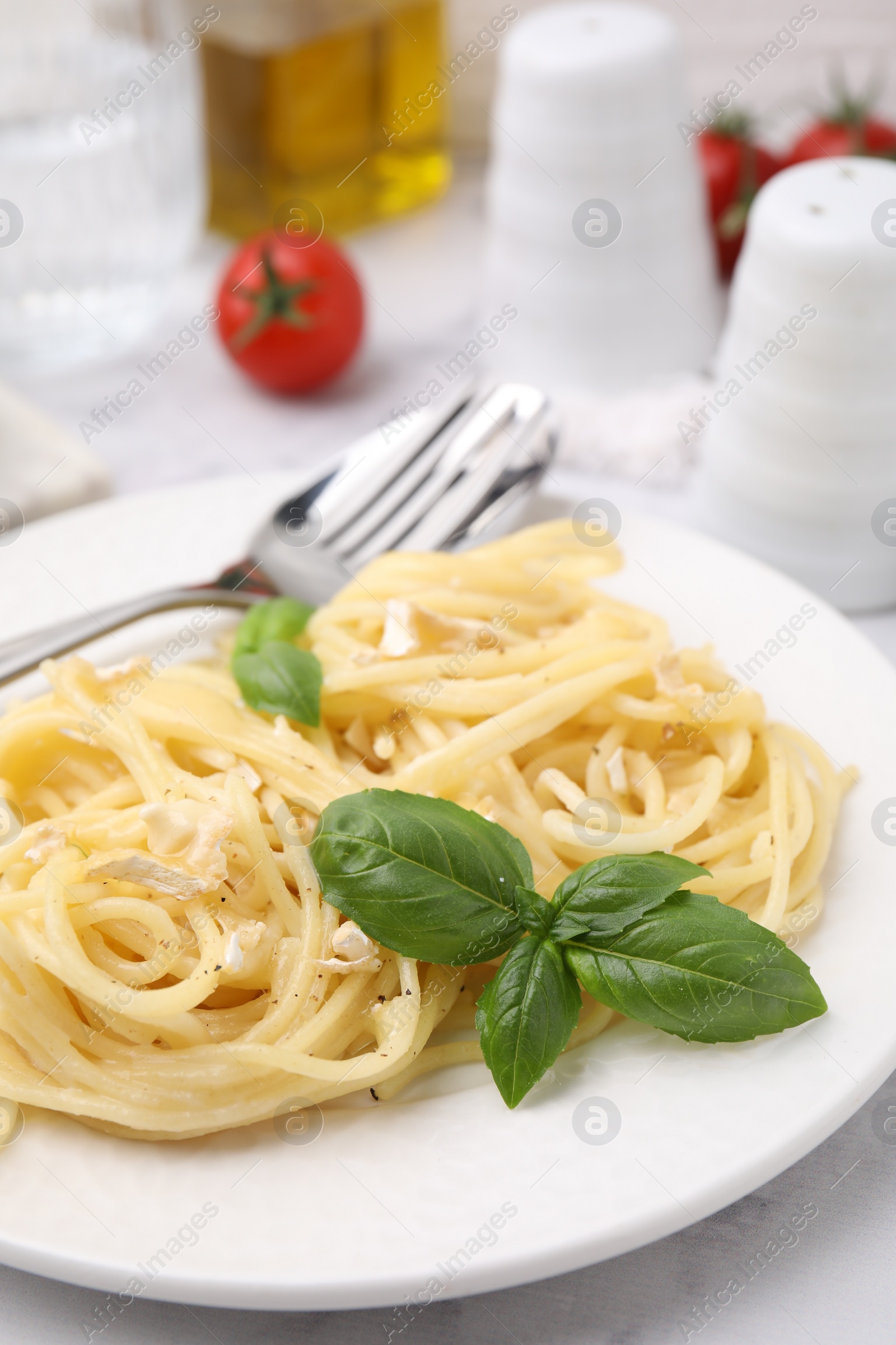 Photo of Delicious pasta with brie cheese and basil leaves on white table, closeup