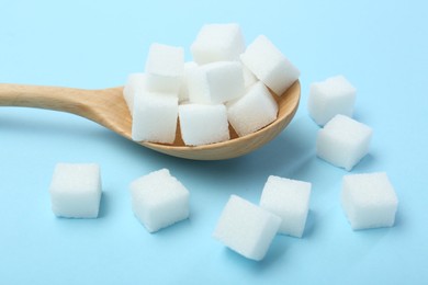 Photo of White sugar cubes and wooden spoon on light blue background, closeup