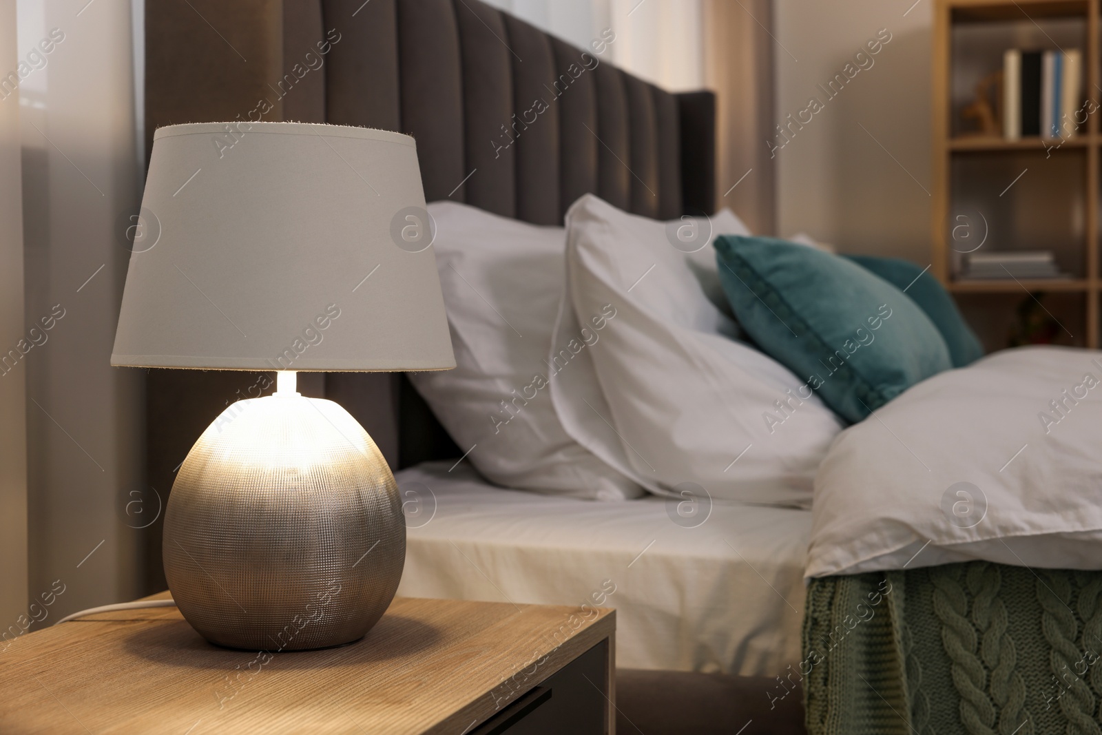 Photo of Lamp on wooden bedside table and comfortable gray bed in bedroom