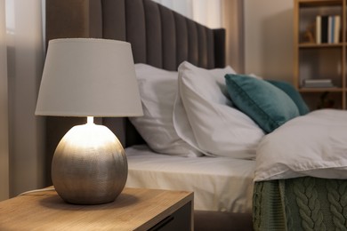 Lamp on wooden bedside table and comfortable gray bed in bedroom