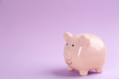 Photo of Piggy bank on violet background. Space for text