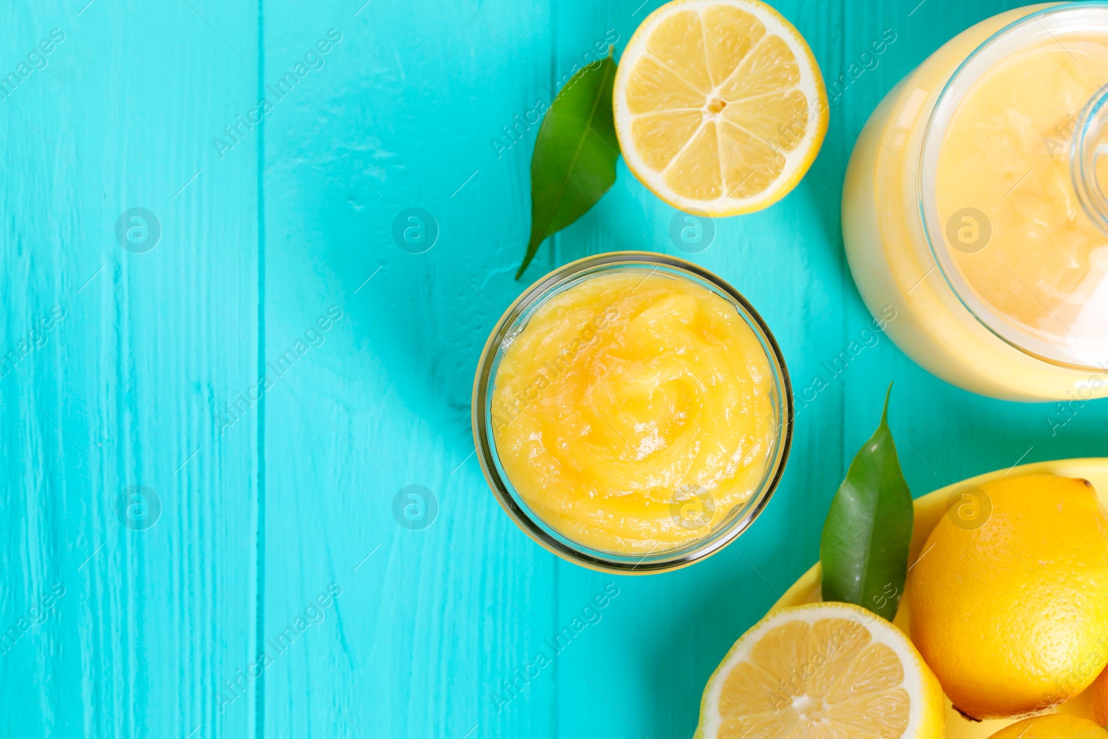 Photo of Delicious lemon curd in jar, fresh citrus fruits and green leaves on light blue wooden table, flat lay. Space for text