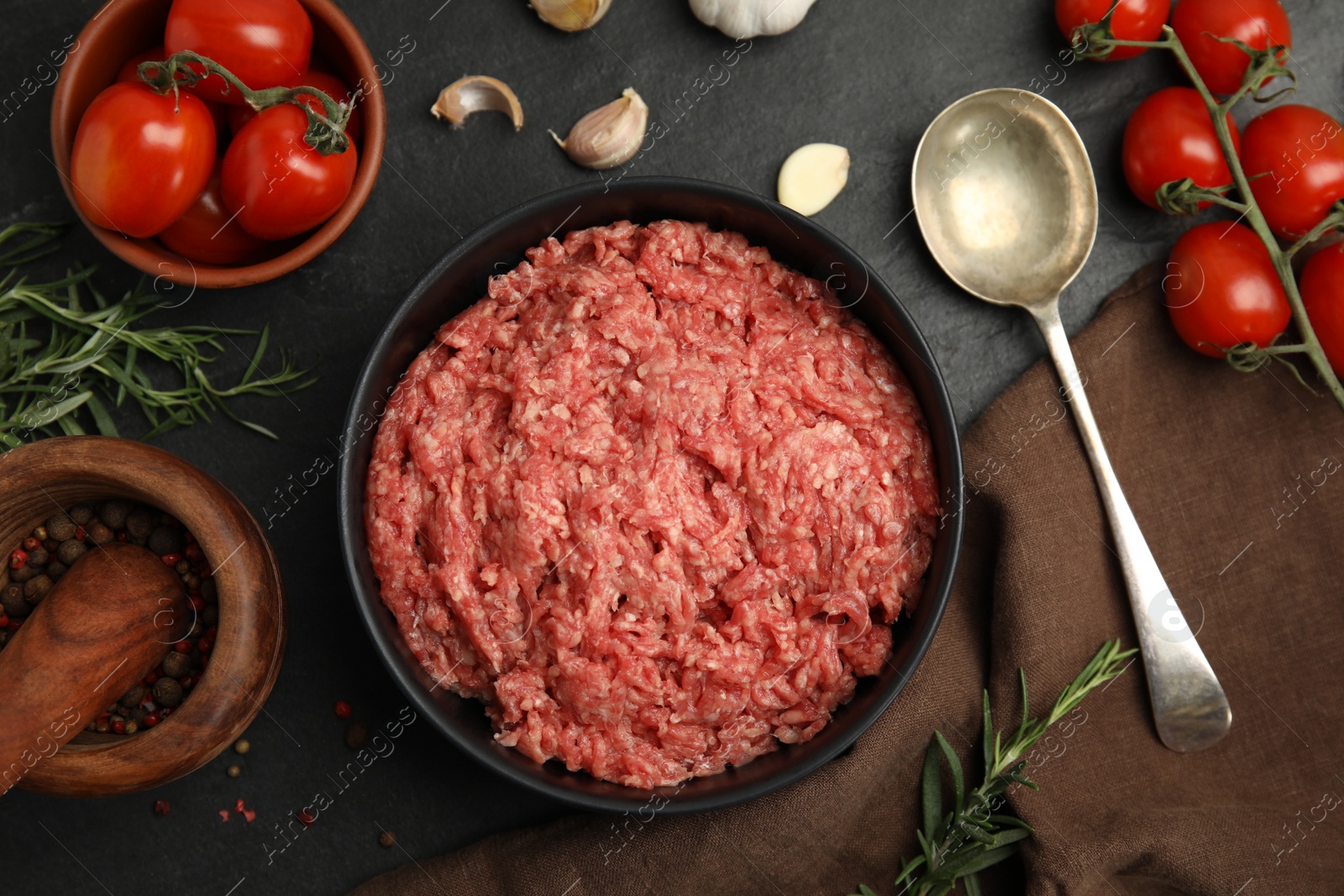 Photo of Fresh minced meat in bowl and other ingredients on black table, flat lay