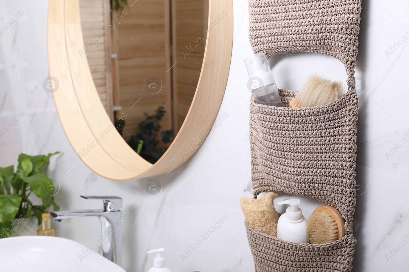 Photo of Storage with essentials hanging near mirror on white marble wall in bathroom. Stylish accessory