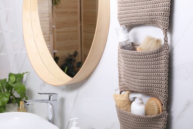 Storage with essentials hanging near mirror on white marble wall in bathroom. Stylish accessory