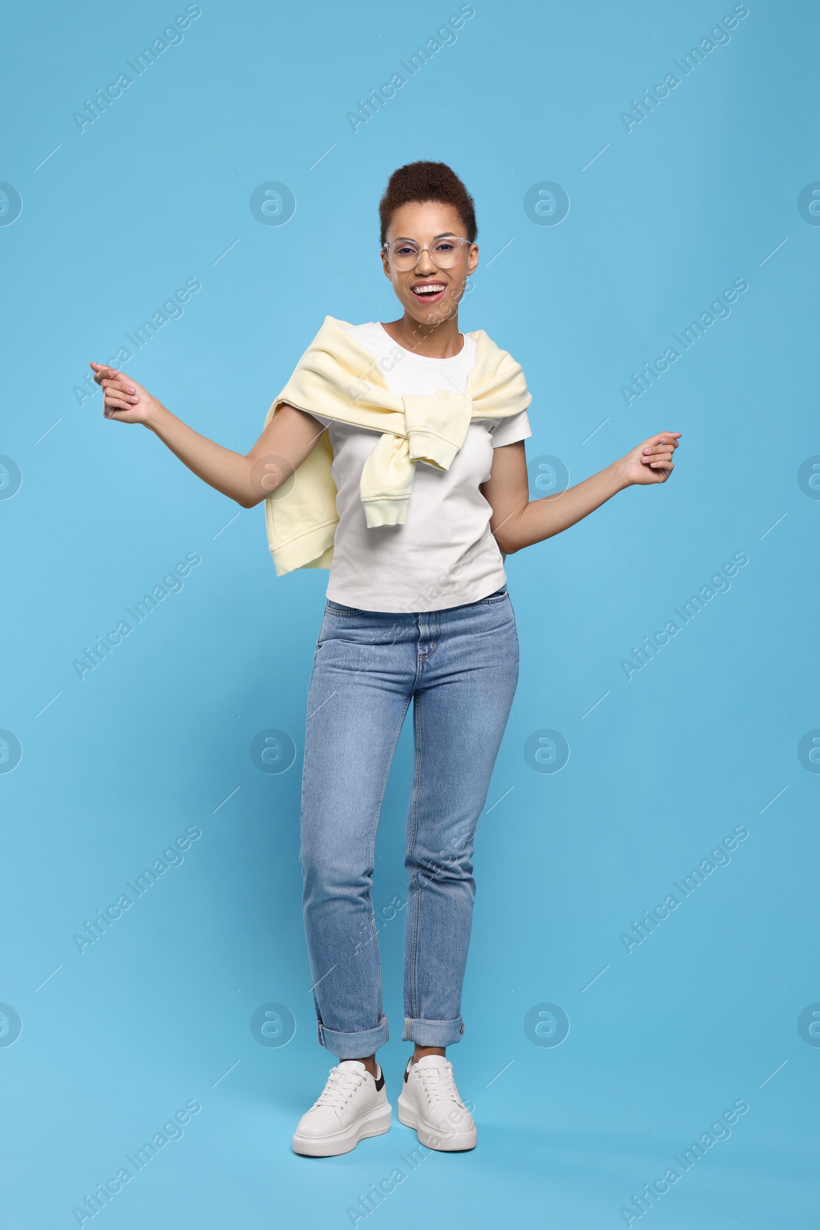 Photo of Happy young woman in stylish eyeglasses dancing on light blue background