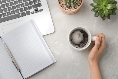 Photo of Young woman with cup of delicious hot coffee at table, top view