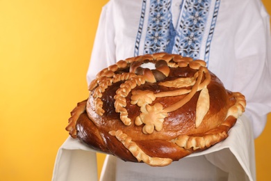 Photo of Woman with korovai on yellow background, closeup. Ukrainian bread and salt welcoming tradition