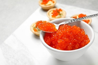 Spoon and bowl with delicious red caviar on board