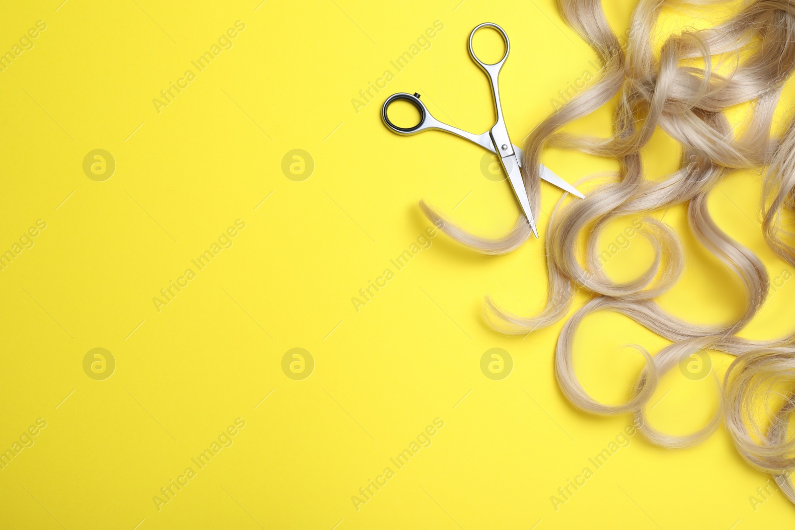 Photo of Professional hairdresser scissors, hair strands and space for text on yellow background, flat lay. Haircut tool