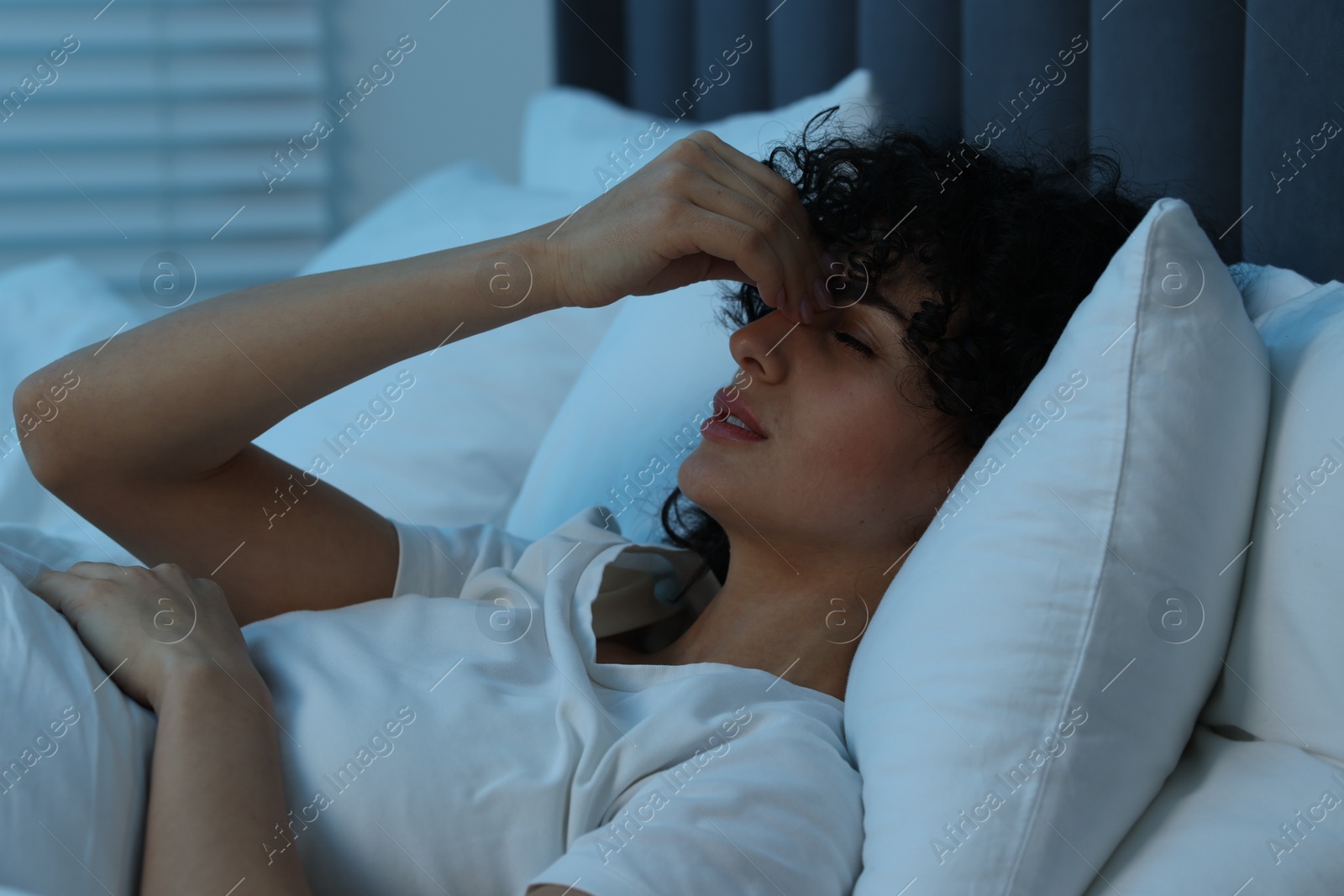 Photo of Young woman suffering from headache in bed at night