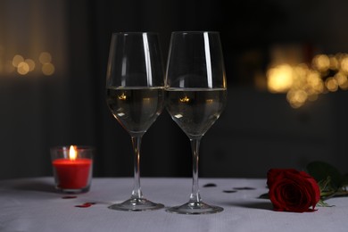 Photo of Glasses of white wine, burning candle and rose flower on grey table against blurred lights. Romantic atmosphere