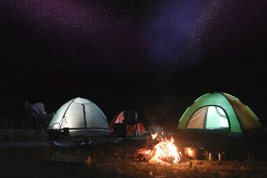 Image of Bonfire near camping tents outdoors at night