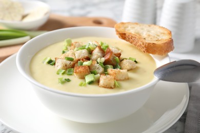 Photo of Tasty potato soup with croutons in bowl and spoon on white table