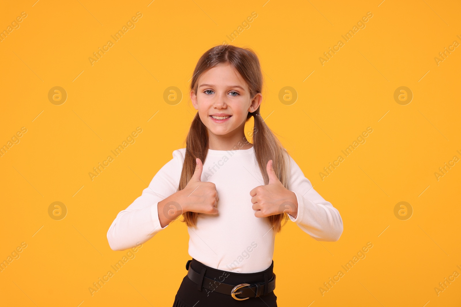 Photo of Happy schoolgirl showing thumbs up on orange background
