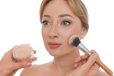 Professional makeup artist applying powder onto beautiful young woman's face with brush on white background, closeup