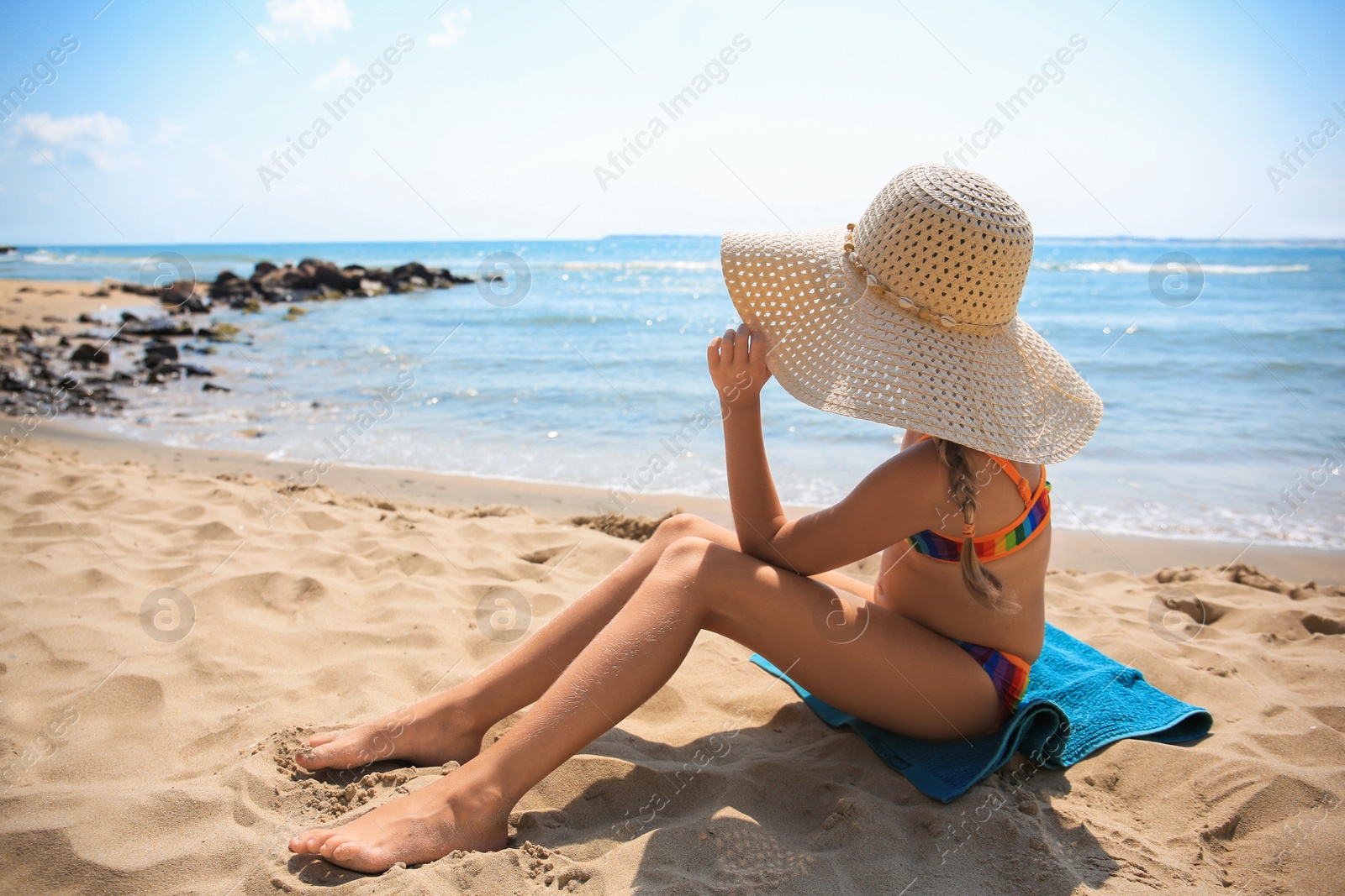 Photo of Little girl in stylish hat on sandy beach near sea