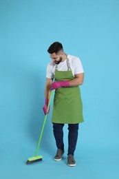 Young man with green broom on light blue background