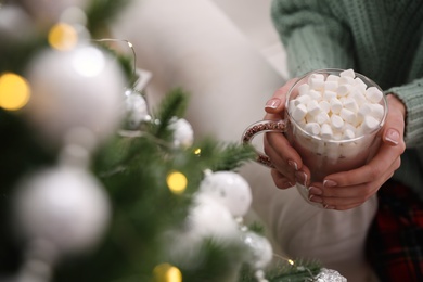 Photo of Woman with cup of delicious hot drink near Christmas tree indoors, closeup. Space for text