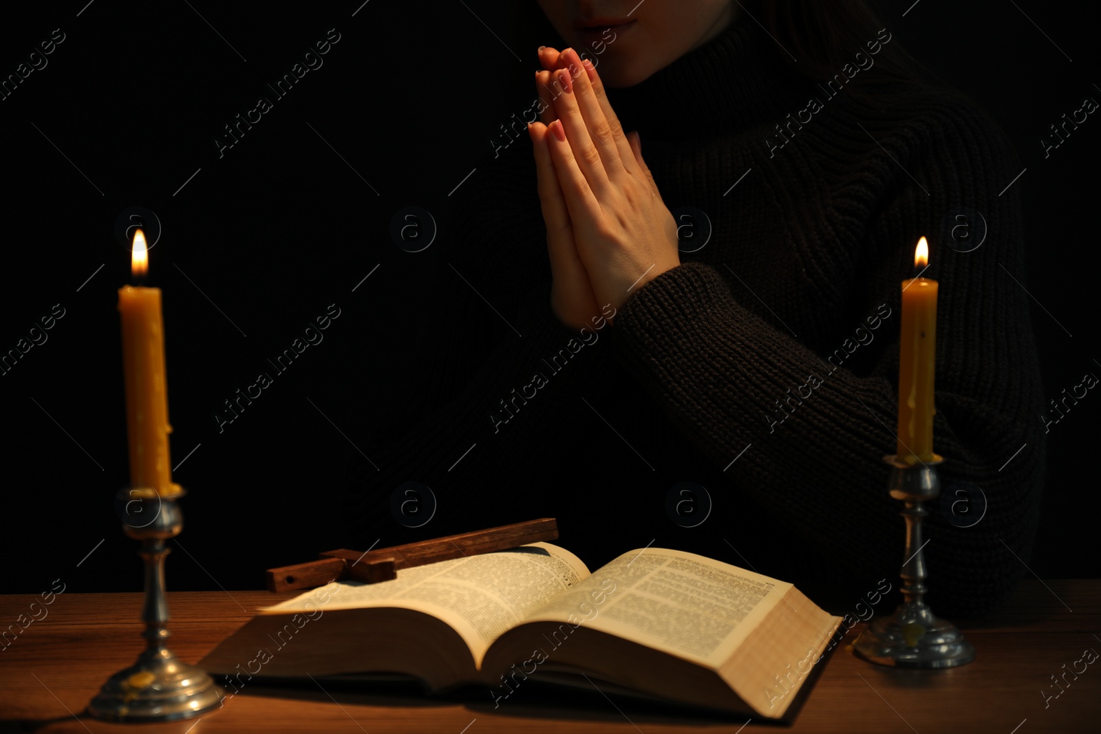 Photo of Woman praying at table with burning candles and Bible, closeup