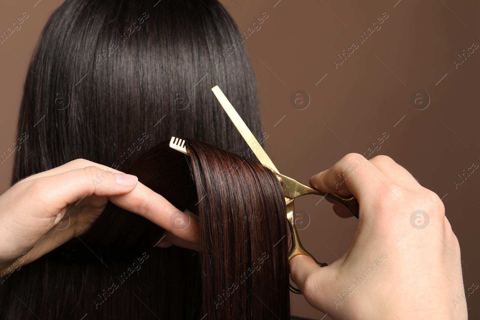 Photo of Hairdresser cutting client's hair with scissors on light brown background, closeup