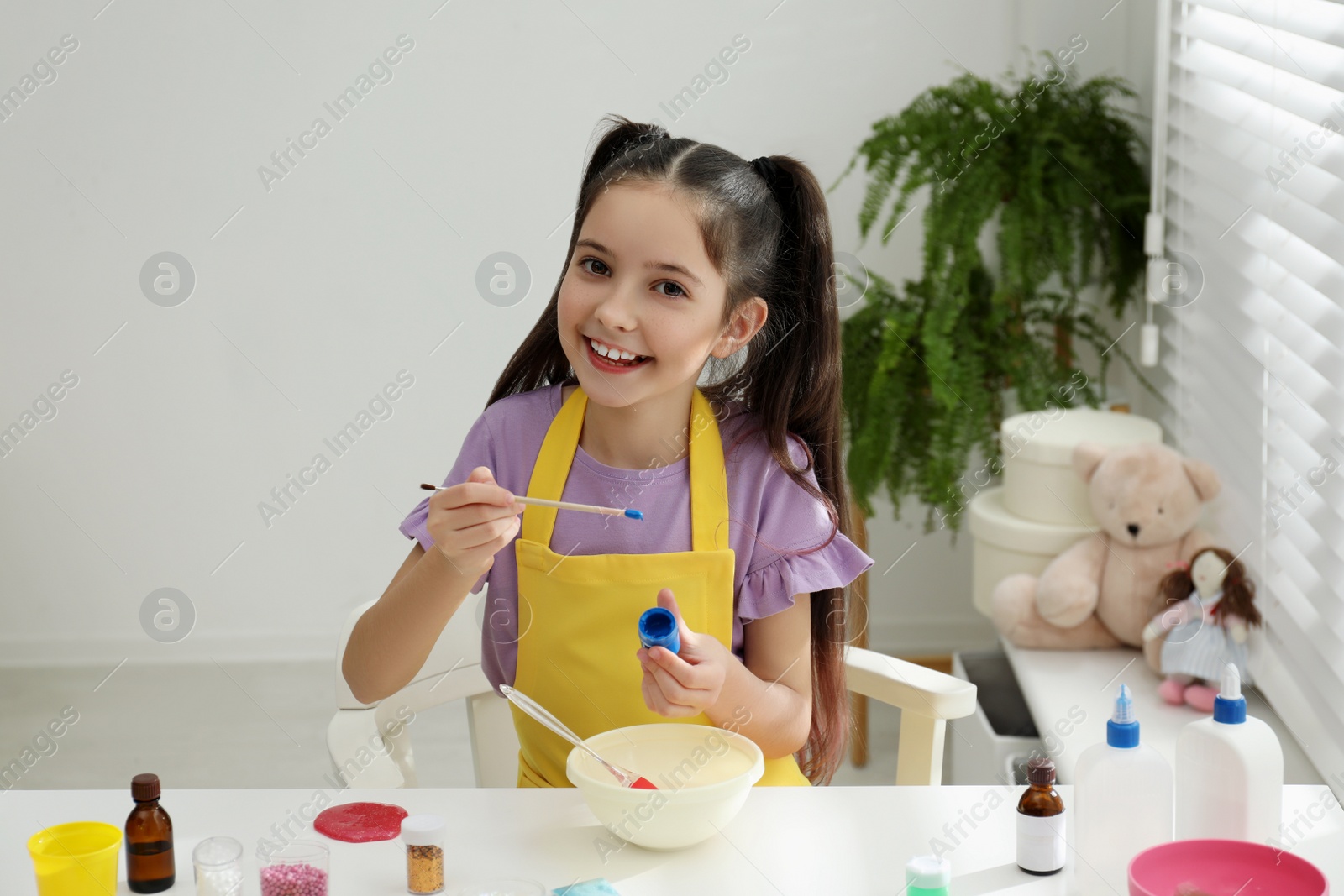 Photo of Cute little girl making homemade slime toy at table in room