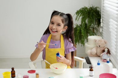 Cute little girl making homemade slime toy at table in room