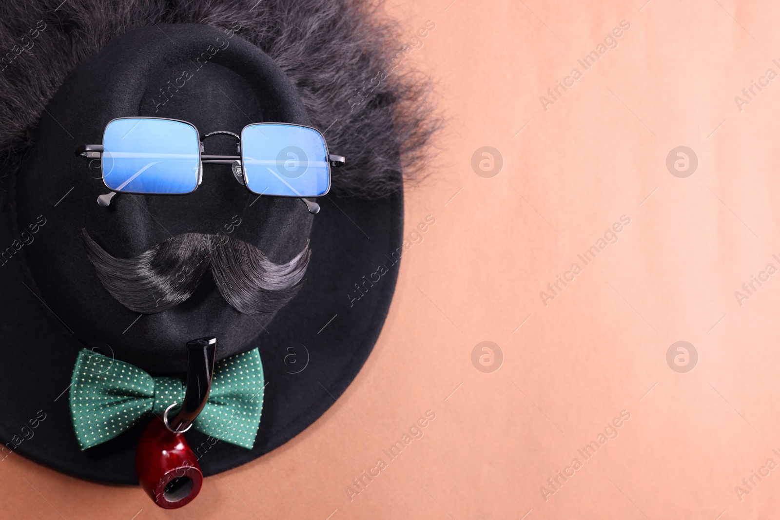 Photo of Man's face made of artificial mustache, sunglasses and hat on brown background, top view. Space for text