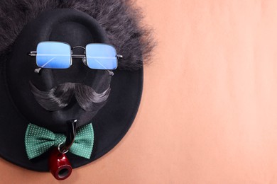 Photo of Man's face made of artificial mustache, sunglasses and hat on brown background, top view. Space for text