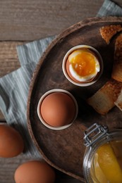 Tasty boiled eggs in cups on wooden table, flat lay