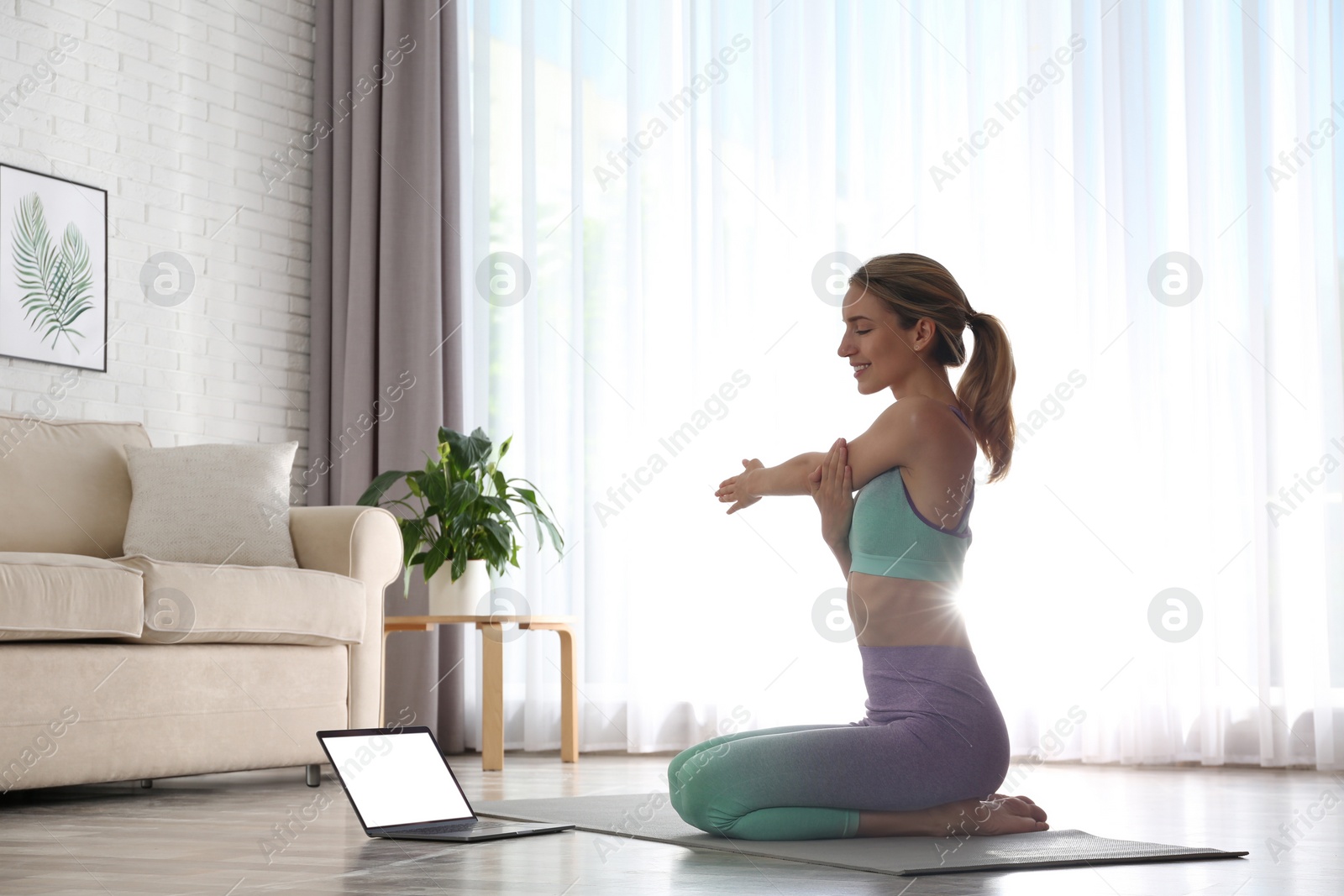 Photo of Woman having online video class via laptop at home. Distance yoga course during coronavirus pandemic