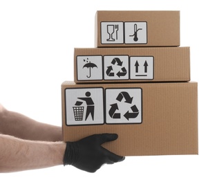 Photo of Courier holding cardboard boxes with different packaging symbols on white background, closeup. Parcel delivery