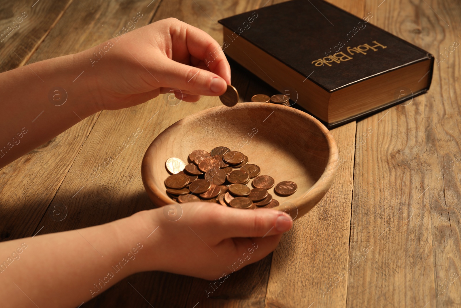 Photo of Donate and give concept. Woman putting coin into bowl at wooden table, closeup