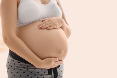 Pregnant woman after application of body cream on blurred background, closeup