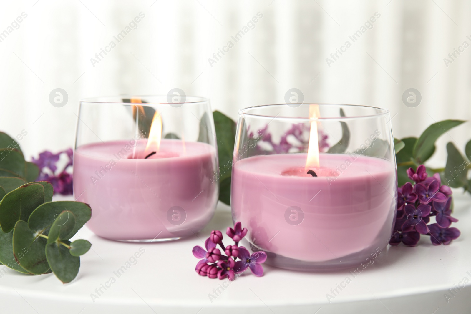 Photo of Burning candles in glass holders and flowers with leaves on white table