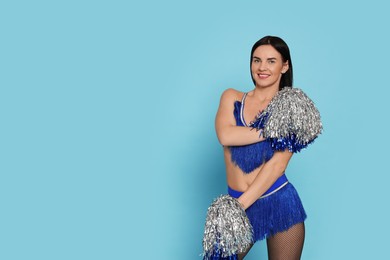 Photo of Beautiful cheerleader in costume holding pom poms on light blue background. Space for text