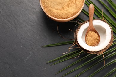 Photo of Spoon with coconut sugar, fruit, bowl and palm leaves on dark textured table, flat lay. Space for text