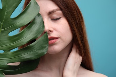 Beautiful woman with freckles and monstera leaf on light blue background, closeup